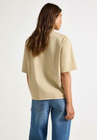 Beige, løs T-shirt med korte ærmer og rund halsudskæring, parret med blå, vide jeans. Stoffet ser blødt ud med en let struktur.