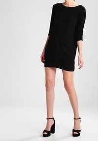 Svartr kortärmad klänning med trekvarts ärmar, rund halsringning och slät textur, i kombination med högklackade svarta platåskor.