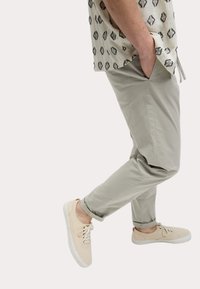 Zapatillas de deporte beige claro, diseñadas con cordones; pantalones gris ajustados con bolsillos laterales; camisa de manga corta con estampado en beige con acentos en negro.