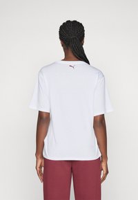 Camiseta blanca de algodón con un corte relajado, mangas cortas y un pequeño logo burdeos en la parte de atrás. Textura suave, diseño simple.