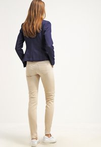 Granatowa dopasowana marynarka w połączeniu z beżowymi, wąskimi spodniami i białymi trampkami. Gładka tkanina i czyste linie definiują nowoczesny, casualowy strój.