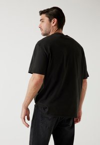 Zwart katoenen t-shirt met korte mouwen, ronde hals en een relaxte pasvorm. De achterkant toont een gladde textuur en een minimalistisch ontwerp.