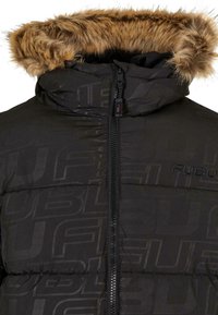 Giacca a vento nera con chiusura a zip, dotata di cappuccio foderato in pelliccia e design con logo impresso. Il materiale sembra liscio e isolato.