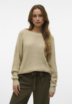 Pull en tricot beige avec un large col bateau, des épaules tombantes et des poignets côtelés, associé à un pantalon taille haute vert olive.