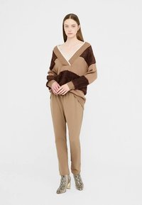 Suéter marrón y texturizado de gran tamaño con cuello en V, combinado con pantalones beige ajustados en los tobillos y botines metálicos con estampado de serpiente.