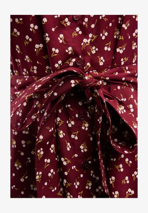 Burgundy dress with small white floral pattern, featuring wrap waist and matching buttons. Soft fabric with a smooth texture.