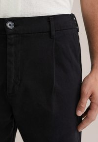 Pantalones negros con una textura de tela suave, que cuentan con un cierre de botón, bolsillos laterales y un corte entallado.