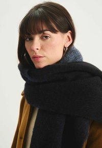 Écharpe tricotée présentant des couleurs bleu marine foncé et gris doux, fabriquée à partir d'un matériau flou et texturé, enroulée de façon élégante autour du cou.