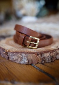 Brown leather belt with a textured finish, featuring a gold-tone metal buckle and minimalist design, resting on a wooden surface.