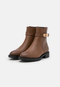 Bottines en cuir marron avec une finition lisse, semelle en caoutchouc noir, bout rond et une sangle décorative avec une boucle dorée.