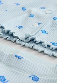 Light blue ribbed fabric with small blue floral patterns, featuring a ruffled hem and white buttons, displayed in a folded arrangement.