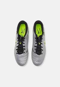 Chaussures de football grises avec un design texturé, des lacets noirs et un intérieur vert fluo vif. Présente un logo Nike sur le côté.