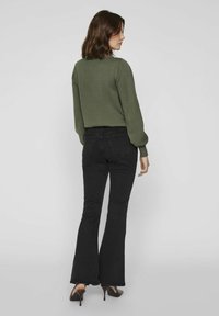 Zaļš adīts džemperis ar garām piedurknēm, apvienots ar melnām plati izgrieztiem džinsiem. Džinsiem ir aizmugurējās kabatas, un tos papildina brūni ar papēdi apavi.