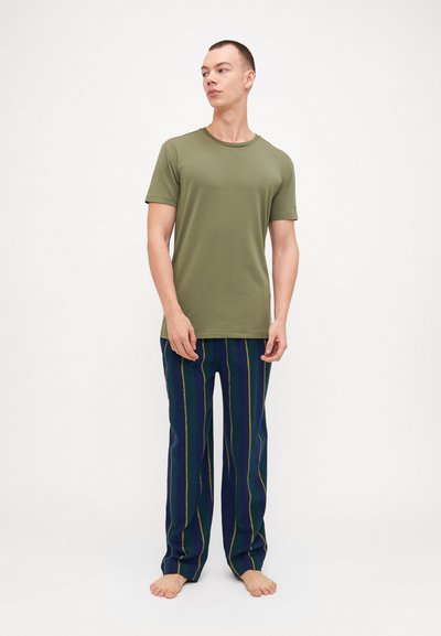Cămașă verde cu mâneci scurte, asortată cu pantaloni navy cu dungi, având linii galbene și verzi. Modelul stă desculț pe un fundal simplu.