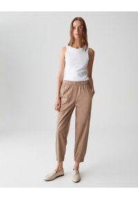 Weißes ärmelloses Oberteil kombiniert mit hellbraunen, taillierten Hosen mit elastischem Bund und seitlichen Taschen. Die Schuhe sind beigen Slips.