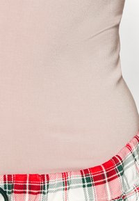 Top rosa claro feito de um tecido liso com uma cintura xadrez vermelha e verde na parte inferior. O xadrez apresenta linhas verticais e horizontais.