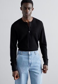 Zwarte langemouwen henley shirt met knopen, gestructureerde stof. Gecombineerd met lichtblauwe denim jeans met een klassieke vijf-pocket ontwerp.