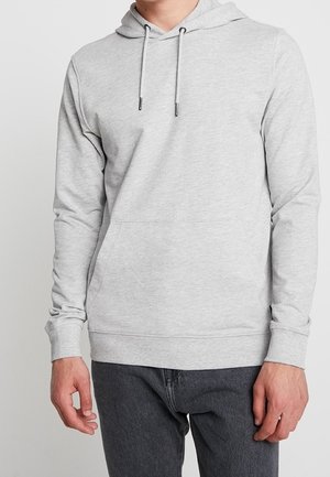 Mann trägt hellgrauen Kapuzenpullover mit Kordeln und Fronttasche, kombiniert mit dunkelgrauer Hose, vor neutralem Hintergrund.