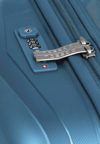 Valigia rigida blu in primo piano con lucchetto approvato dalla TSA, superficie testurizzata e zip metallica con doppio gancio.