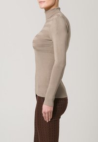 Beige høyhalset topp med ribbet tekstur og subtile horisontale striper; tettsittende design med lange ermer og buet nederkant.