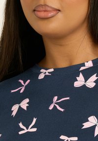 Granatowa bluzka z wzorem różowych i paskowanych kokardek. Okrągły dekolt, krótkie rękawy, miękka faktura tkaniny. Idealna do codziennych stylizacji.