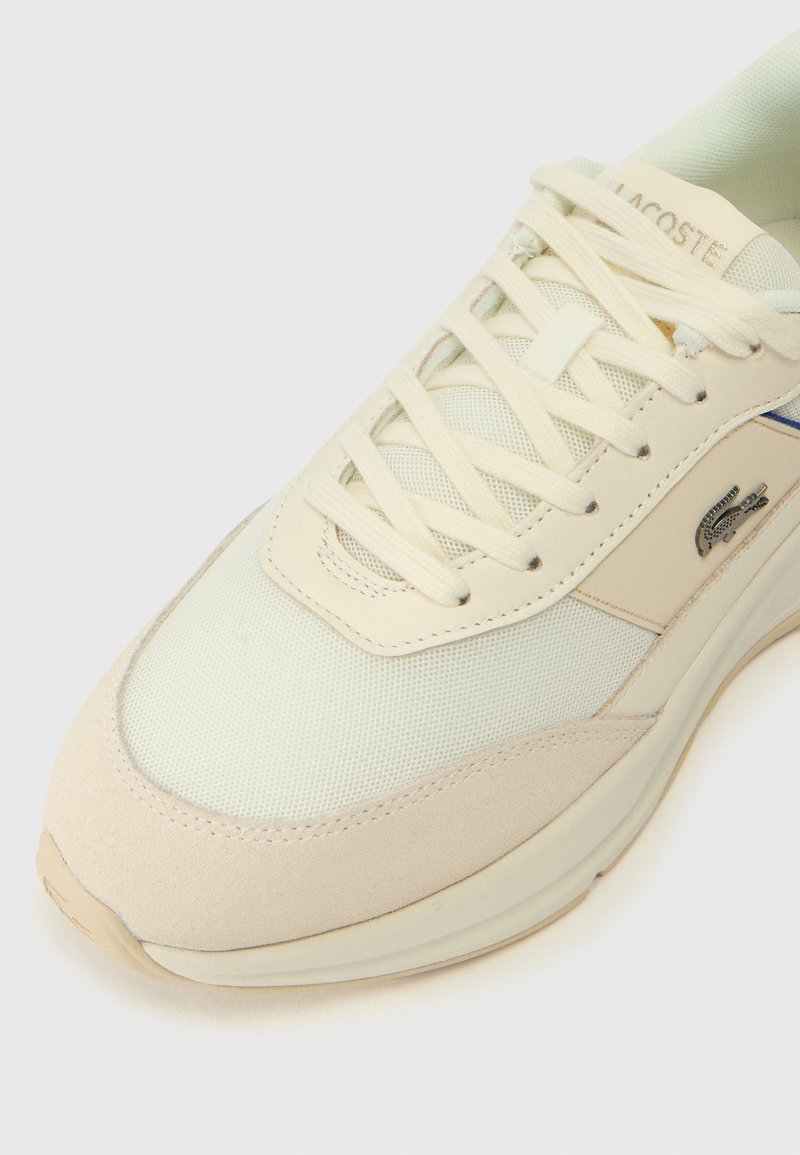 Beige Sneaker mit Mesh- und Wildleder-Panels, runder Spitze, cremefarbenen Schnürsenkeln, blauer Akzentlinie und silbernem Logo. Glatte Textur und gepolsterte Sohle.