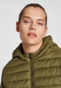 Olivengrüne, gefütterte Kapuzenjacke mit strukturiertem, gestepptem Design und einem Reißverschluss vorne. Leicht, mit einem entspannten Schnitt und verstellbarer Kapuze.