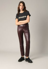 Zwarte T-shirt met "lovers" in crème erop gedrukt, gecombineerd met glanzende, bordeauxrode neplederen broeken. Zwarte veterschoenen maken de outfit af.