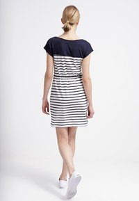 Vestido a rayas en navy y blanco con mangas cortas, cintura elástica y un diseño casual, combinado con zapatillas blancas, visto desde atrás.
