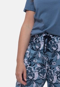 Casual outfit met een blauwe t-shirt en een blauw-witte, loszittende broek met bloemenpatroon, voorzien van een elastische tailleband en een aantrekkoord.