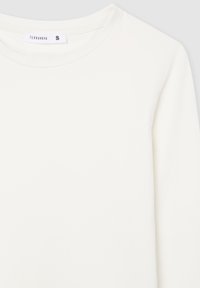 Primo piano di una maglietta bianca a maniche lunghe con scollo rotondo, con etichetta "Terranova" e tag di taglia piccola sul colletto.