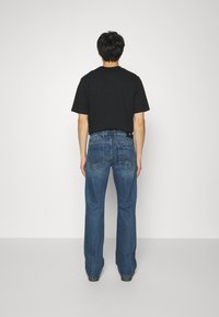 Camisa negra de manga corta y jeans de mezclilla acampanados azules vistos desde atrás. Los jeans tienen bolsillos traseros con costuras distintivas y un leve desgastado.