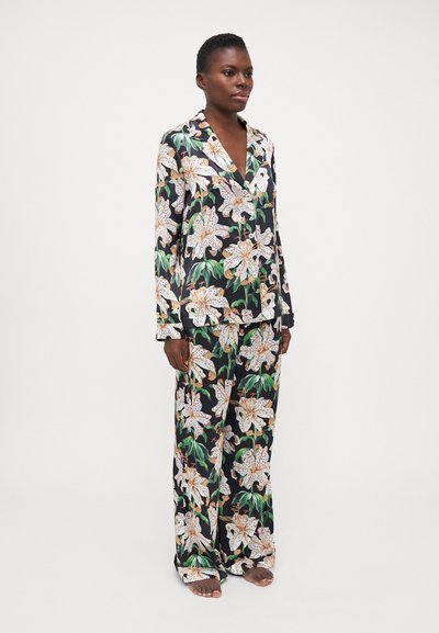 Black floral sleep set made of satin features large white lilies and vibrant green leaves. The tailored design includes a notched collar and wide pants.