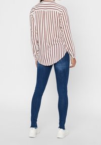 Randig långärmad skjorta i kräm och rost, med en böjd fåll och knappdetaljer, tillsammans med mörkblå tajta jeans och vita sneakers.