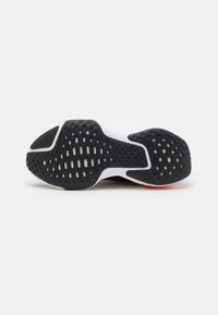 Semelle de chaussure en caoutchouc noir avec des motifs de grip texturés et une semelle intermédiaire blanche. Présente un détail de logo discret près du talon et des rainures pour l'adhérence.