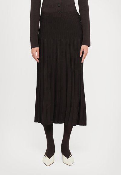 Schwarzer, plissierter Midikleid aus Strickstoff, ausgestattet mit einem gerippten Bund, kombiniert mit dunklen Strumpfhosen und spitzen weißen Schuhen.