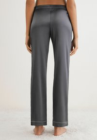 Grijze satijnen pyjamabroek met een relaxed fit, elastische tailleband en contrasterende witte piping bij de pijpen. Gladde textuur en minimalistisch ontwerp.