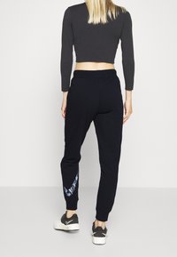 Svart kortärmad långärmad topp som kombineras med marinblå joggingbyxor med ett blåt mönstrat accent på vänster ben och svarta sportskor.
