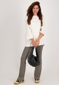 Witte top met brede mouwen, gemusterde grijze flarebroek, zwarte tas met zilveren studs en zwart-witte schoenen op een neutrale achtergrond.