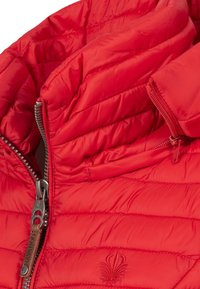 Veste matelassée rouge avec une texture en coussin, dotée d'un col montant, d'une fermeture éclair métallique et d'un logo brodé à l'avant.