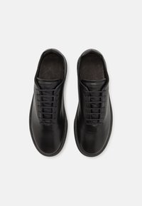 Black leather shoes with a smooth texture, round toe, and minimalistic design. Features flat laces and a clean, understated silhouette.