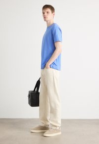 Modrá bavlnená tričko, voľný strih, skombinovaná s béžovými širokými nohavicami. Béžové tenisky a čierna kabelka cez rameno dotvárajú outfit.