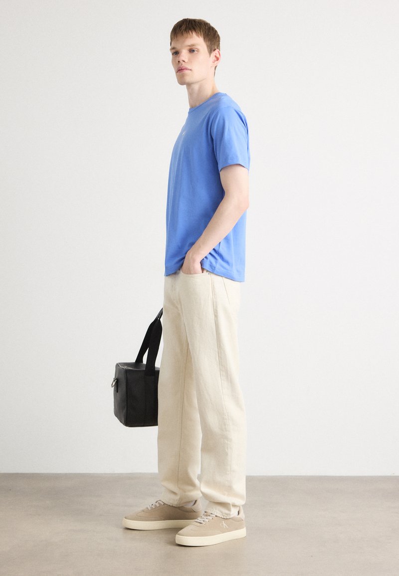 Niebieska bawełniana koszulka, luźny krój, zestawiona z beżowymi spodniami o szerokich nogawkach. Beżowe sneakersy i czarna torebka na ramię dopełniają stylizację.