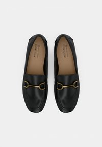 Mocassins noirs en cuir végan avec détail mors doré, bout carré, et semelles intérieures beiges marquées "CALL IT SPRING BELDGAM VEGAN".