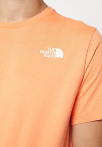 Pomarańczowa koszulka z krótkim rękawem, wykonana z gładkiej bawełny, z białym logo na lewej piersi, z klasycznym okrągłym dekoltem.