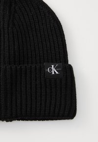 Fekete kötött sapka bordás textúrával és hajtott szegéllyel. A szegélyen egy téglalap alakú címke található, amelyen a "Calvin Klein Jeans" logó látható.