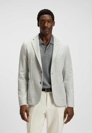 Hellegrauer kariierter Blazer mit einem strukturierten Muster, einreihiger Schnitt, Spitzrevers und zwei Fronttaschen, getragen über einem grauen Poloshirt.