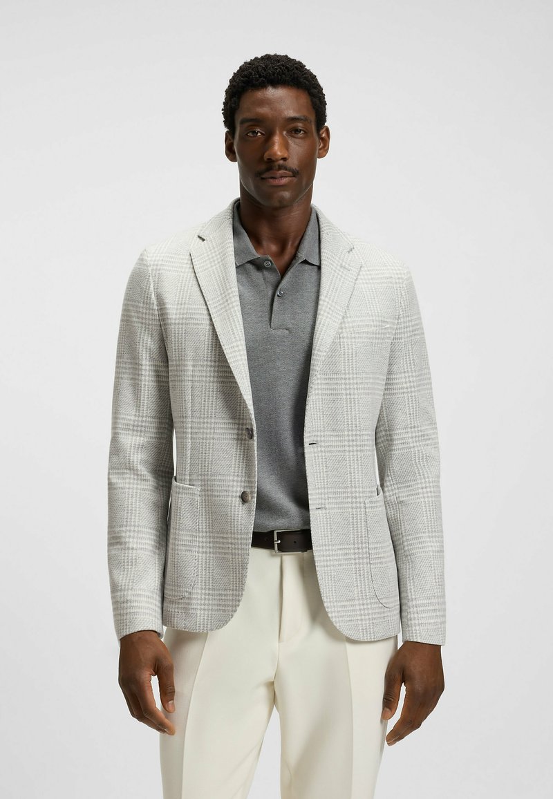 Jasnoszary blezer w kratę z teksturowanym wzorem, jednorzędowy krój, klapy w szpic i dwie przednie kieszenie, noszony na szarym polo.