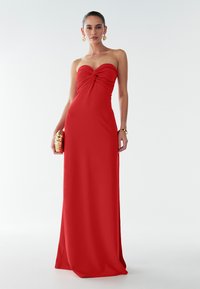 Rode vloerlange jurk met een strapless ontwerp en een samengevoegde knoopdetail bij de buste. Glanzende stof met een getailleerde pasvorm. Gouden clutch met textuur.