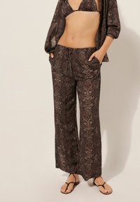 Pantalones de pierna ancha con estampado de serpiente marrón, con cinturilla elástica y bolsillos, combinados con un top corto a juego. Tejido ligero y texturizado.